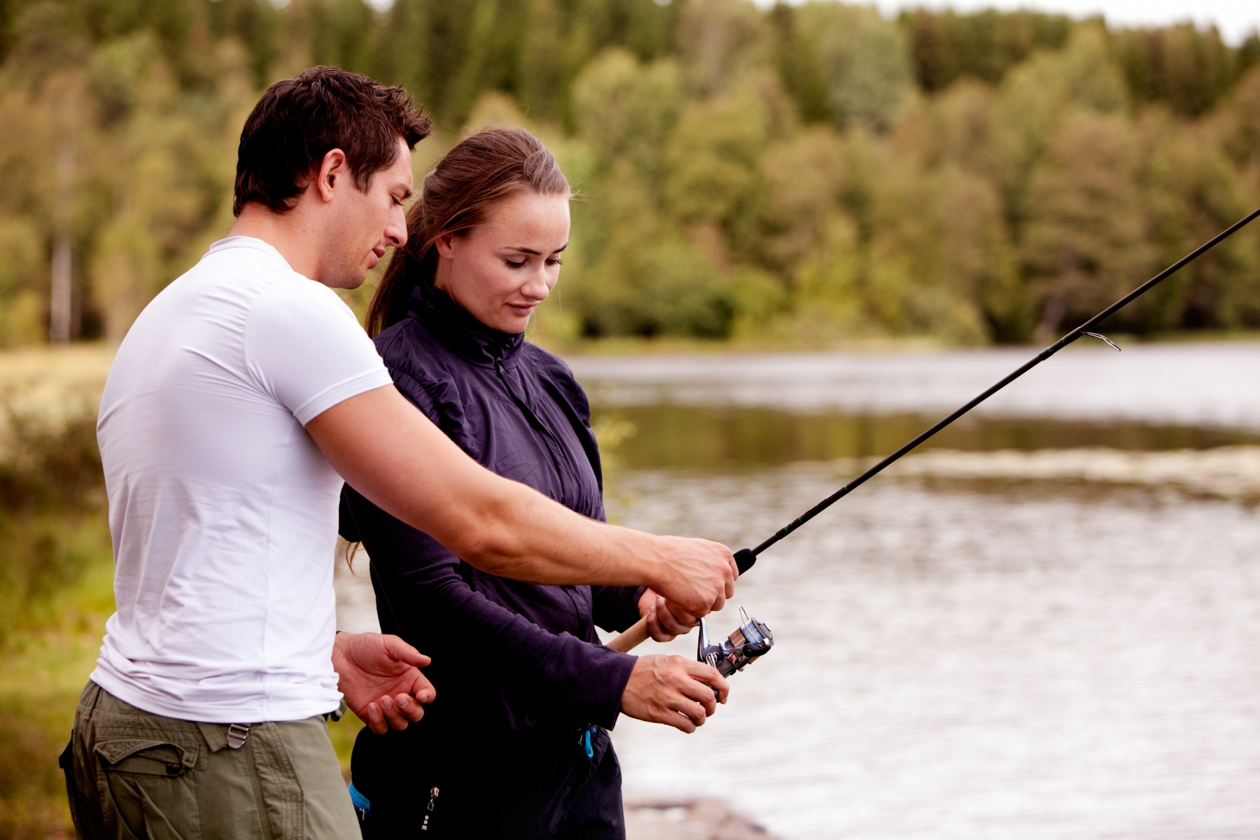 A man explaining how to hold a fishing rod for a woman at a lake.