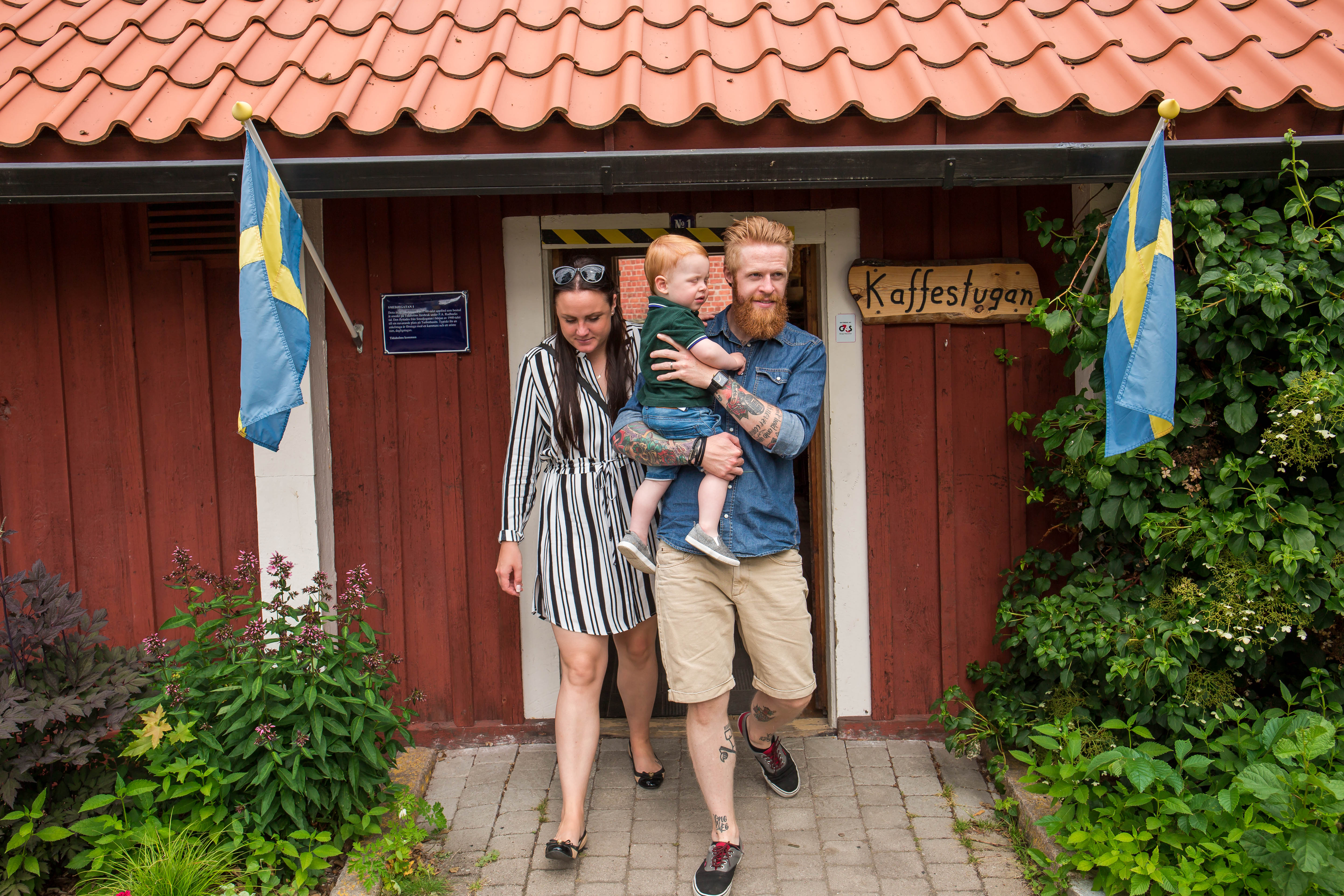 A man holding a child in his arms and a woman going out of the coffee house at Turbinhusön in Tidaholm on a summer day.