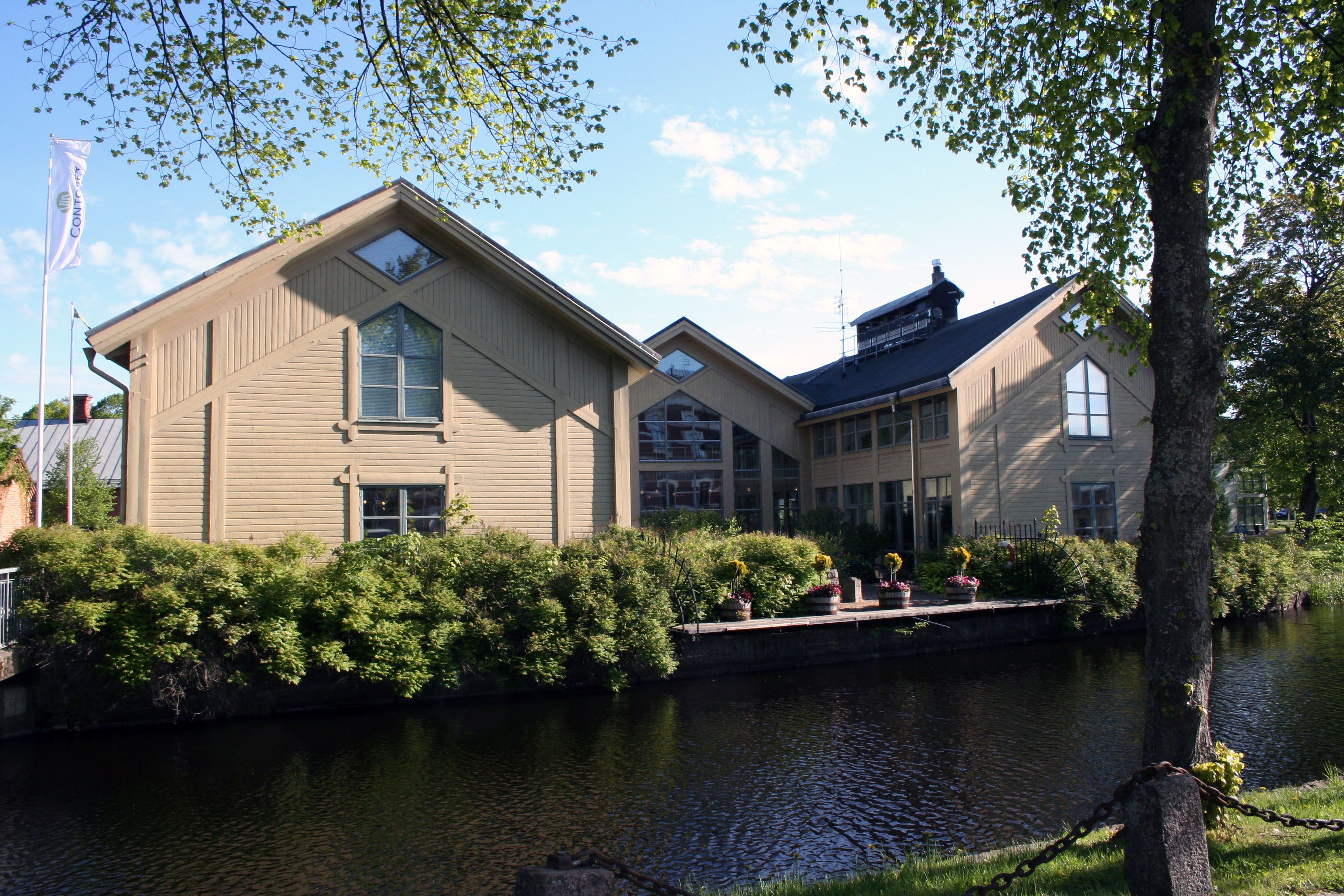 View of the Marbodal Center, a beige wooden building on Vulcan island in the middle of Tidaholm with the river Tidan in front.