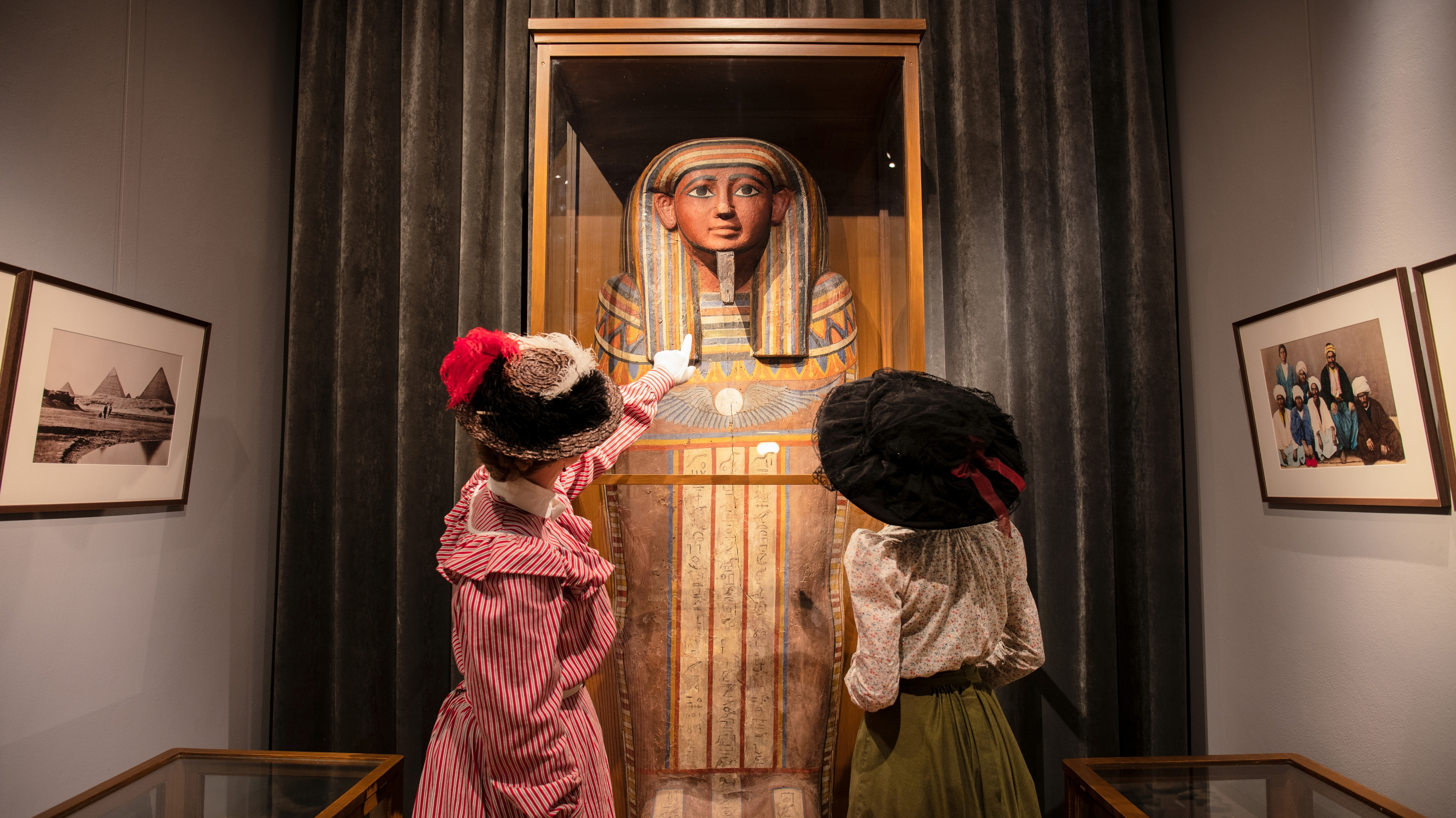 Två kvinnor i hattar tittar på en sarkofag