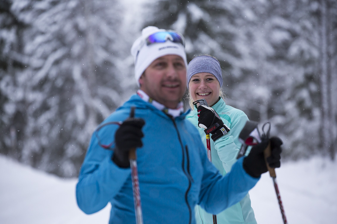 A girl and guy dressed in cross-country ski equipment checking into the camera.