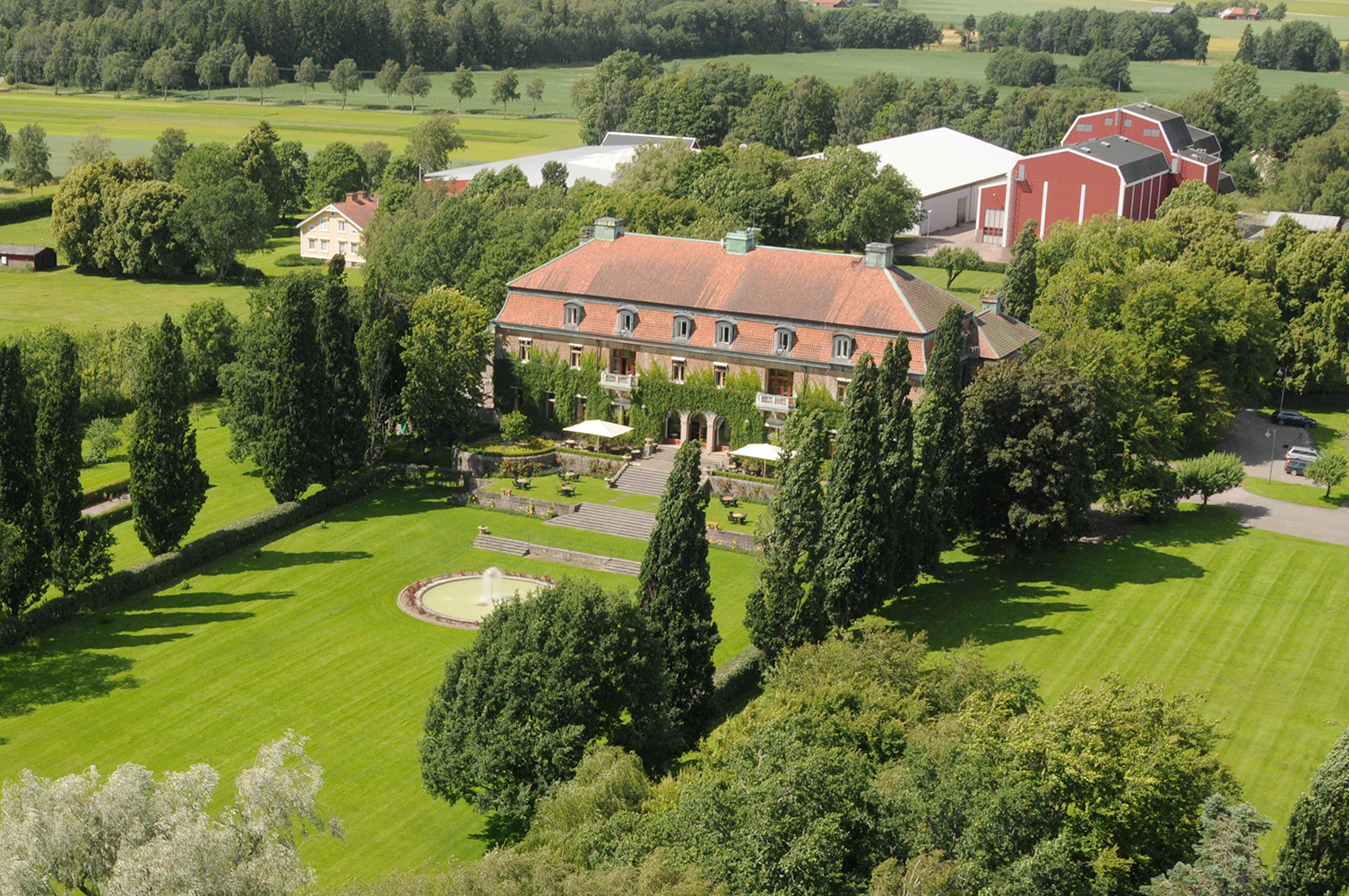 An aerial view where you see a castle. Trees grow all around and fields spread out.
