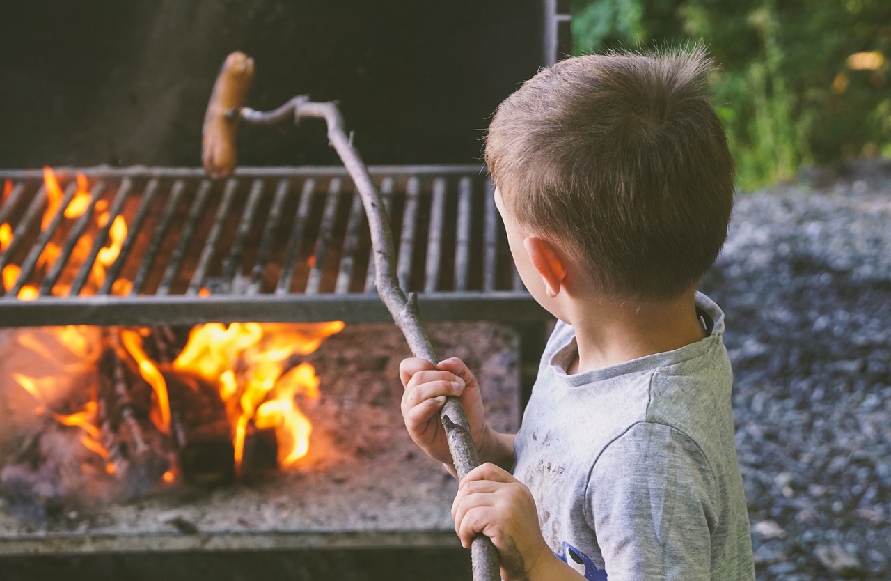 A boy barbecueing a hot dog over an open fire